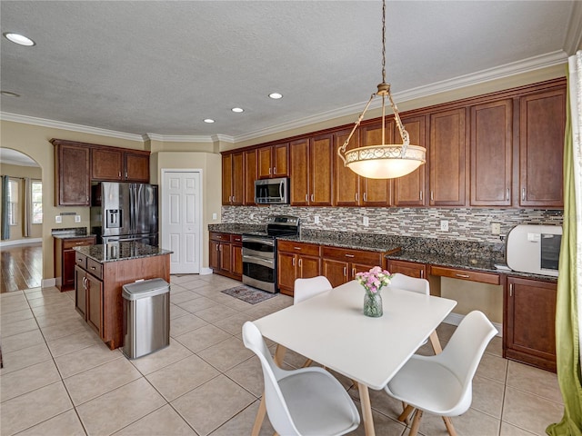 kitchen featuring light tile patterned floors, a center island, arched walkways, appliances with stainless steel finishes, and backsplash
