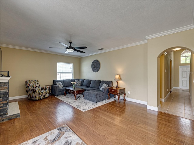 living area with crown molding, arched walkways, a textured ceiling, a ceiling fan, and wood finished floors