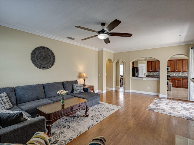 living room featuring arched walkways, light wood-type flooring, ornamental molding, and ceiling fan