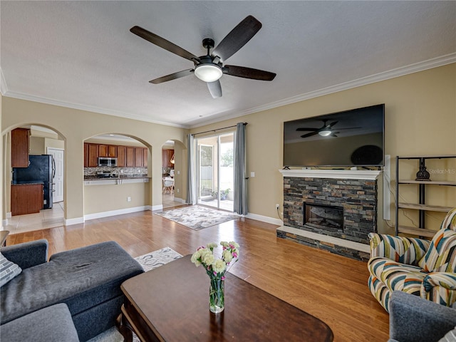 living area featuring arched walkways, a fireplace, light wood finished floors, and a ceiling fan
