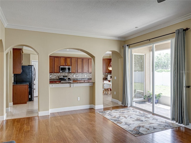 kitchen with dark countertops, brown cabinets, stainless steel appliances, backsplash, and light wood-style flooring