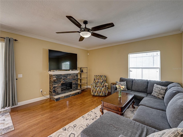 living area featuring a fireplace, a textured ceiling, ornamental molding, a ceiling fan, and wood finished floors