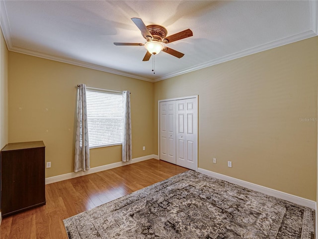 unfurnished bedroom with light wood-type flooring, a closet, crown molding, and baseboards