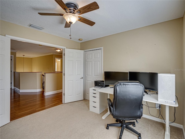 office space with a textured ceiling, a ceiling fan, visible vents, light carpet, and baseboards