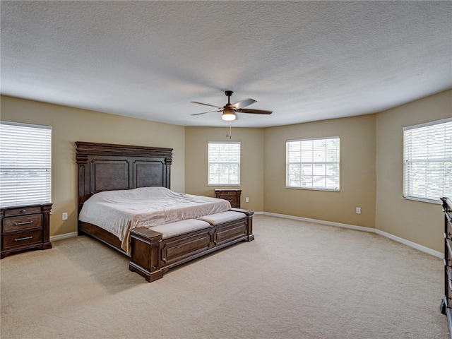 bedroom with a textured ceiling, light colored carpet, baseboards, and a ceiling fan
