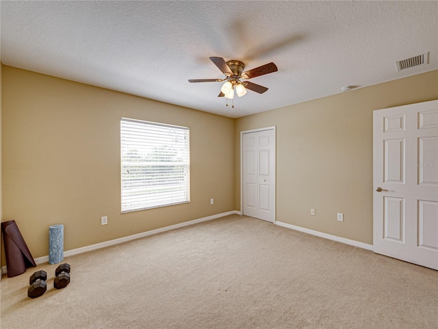 unfurnished bedroom featuring visible vents, baseboards, a ceiling fan, a textured ceiling, and light colored carpet