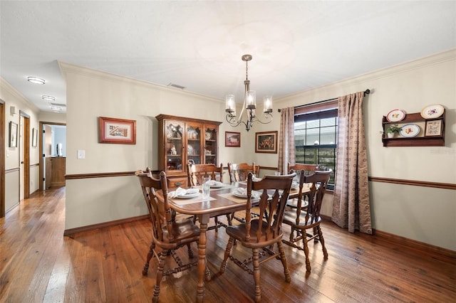 dining room featuring a notable chandelier, ornamental molding, visible vents, and hardwood / wood-style flooring