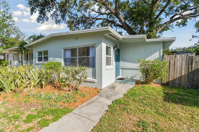 view of front of house with concrete block siding, fence, and a front yard