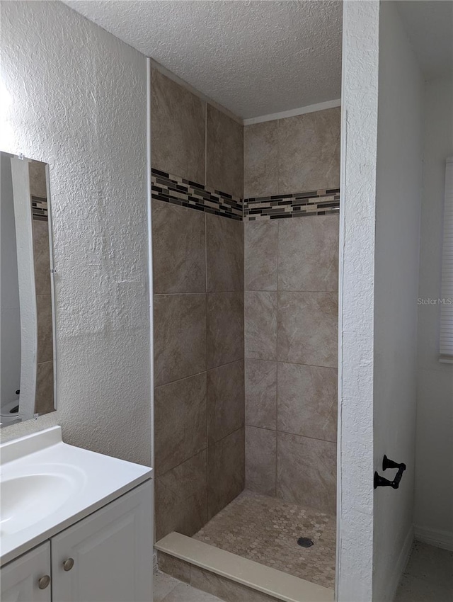full bathroom with a textured wall, vanity, a textured ceiling, and a tile shower