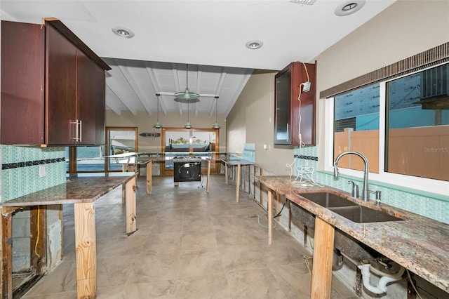 366 La Hacienda Dr, Indian Rocks Beach, FL 33785 - kitchen featuring ceiling fan, light stone counters, beam ceiling, a sink, and glass insert cabinets