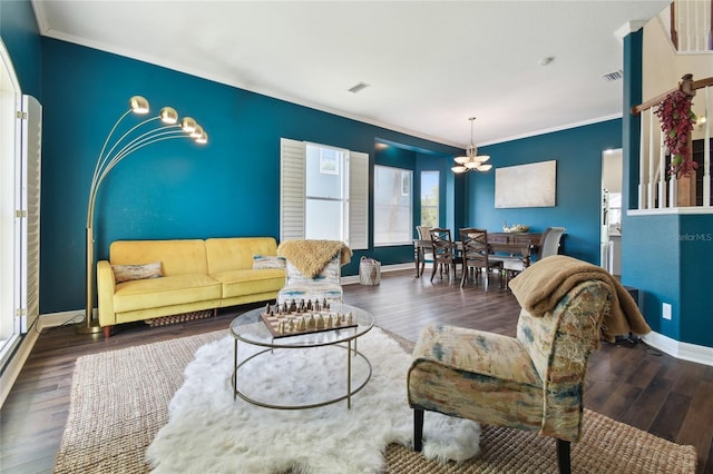 living room with wood finished floors, visible vents, ornamental molding, baseboards, and a chandelier