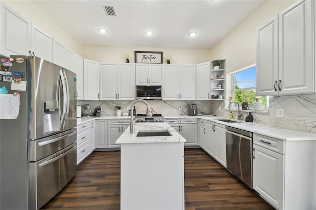 kitchen with stainless steel appliances, dark wood-style floors, a sink, light stone counters, and an island with sink