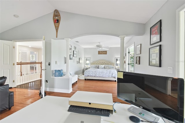 bedroom featuring arched walkways, vaulted ceiling, wood finished floors, and ornate columns