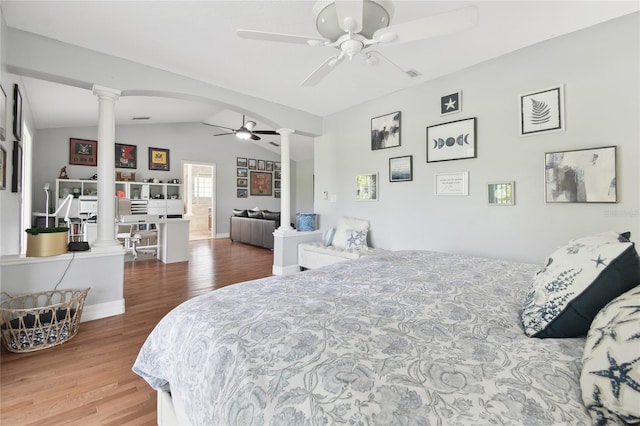 bedroom featuring vaulted ceiling, a ceiling fan, wood finished floors, arched walkways, and decorative columns