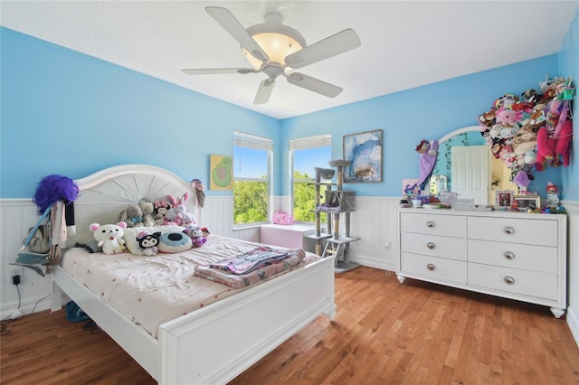 bedroom with light wood-type flooring, a wainscoted wall, and a ceiling fan