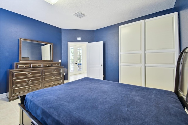 bedroom featuring tile patterned floors, french doors, a textured ceiling, visible vents, and a textured wall