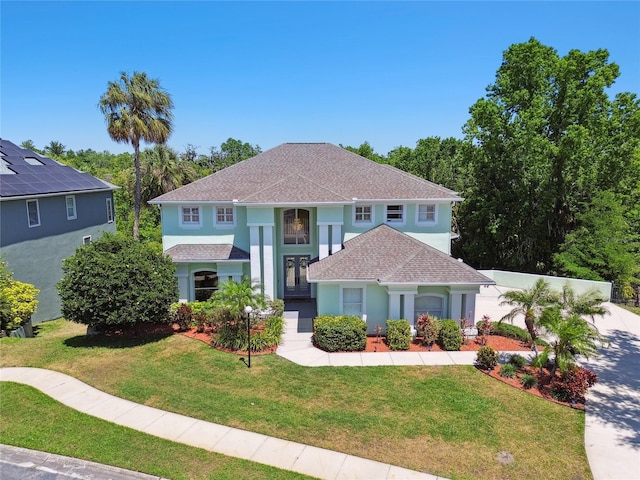 mediterranean / spanish-style home with a shingled roof, a front yard, and stucco siding