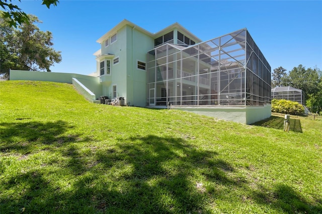 back of house with stucco siding, a lawn, and a lanai