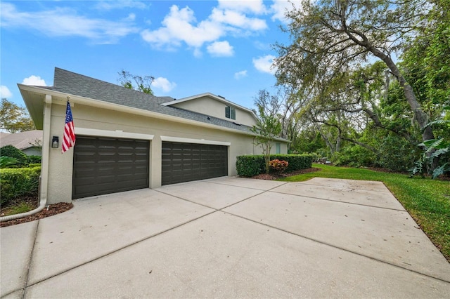 view of side of home with a shingled roof, driveway, stucco siding, and an attached garage