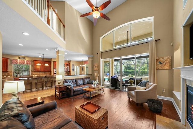living area featuring baseboards, ceiling fan, a glass covered fireplace, and light wood finished floors