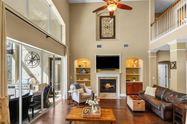 living area featuring dark wood finished floors, visible vents, a tile fireplace, built in features, and ceiling fan