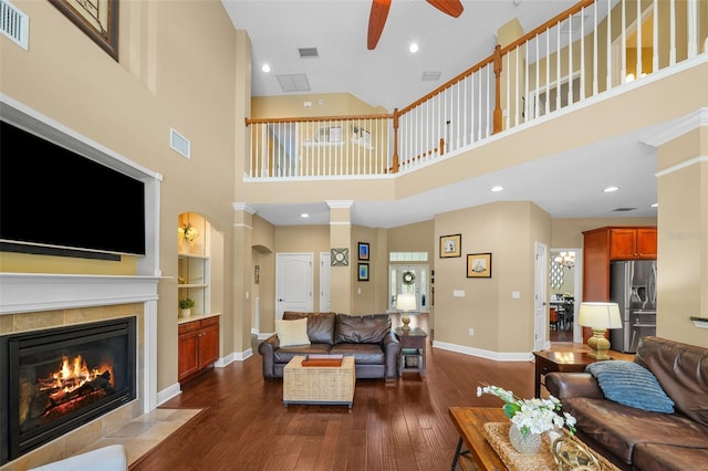 living room featuring dark wood-style flooring, baseboards, visible vents, a tiled fireplace, and a ceiling fan