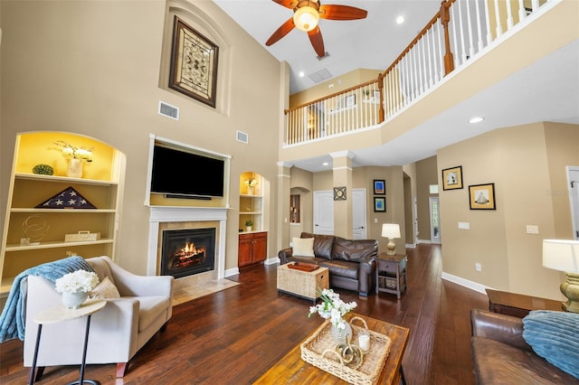 living room with baseboards, hardwood / wood-style flooring, visible vents, a tiled fireplace, and a ceiling fan