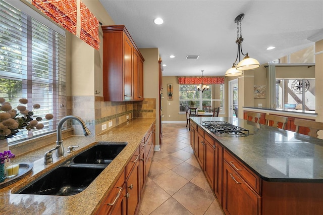 kitchen with gas cooktop, dark stone countertops, a chandelier, backsplash, and a sink