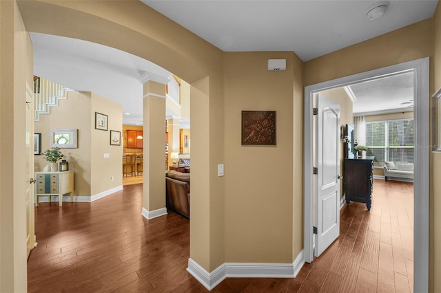 hallway with wood-type flooring, decorative columns, arched walkways, and baseboards
