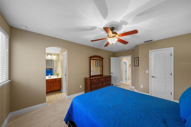 bedroom with visible vents, baseboards, light carpet, arched walkways, and ensuite bath