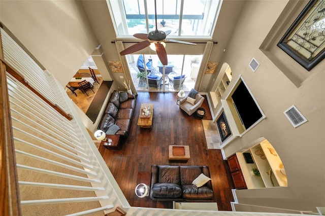 living room with a ceiling fan, a towering ceiling, wood finished floors, and visible vents