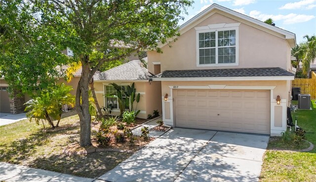 traditional home with roof with shingles, central AC unit, driveway, an attached garage, and stucco siding