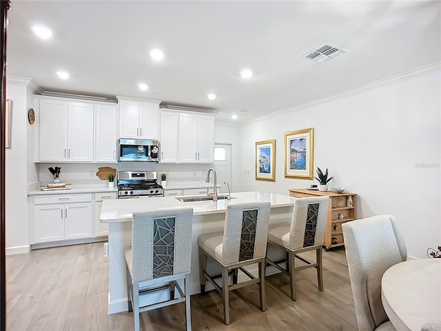 17228 Holly Well Ave, Wimauma, FL 33598 - kitchen with appliances with stainless steel finishes, ornamental molding, light wood-style flooring, a breakfast bar, and a center island with sink