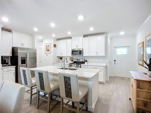 17228 Holly Well Ave, Wimauma, FL 33598 - kitchen featuring stainless steel appliances, crown molding, a kitchen bar, a kitchen island with sink, and light wood-type flooring