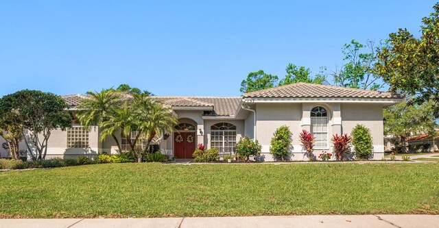 mediterranean / spanish home featuring stucco siding, a front lawn, and a tiled roof