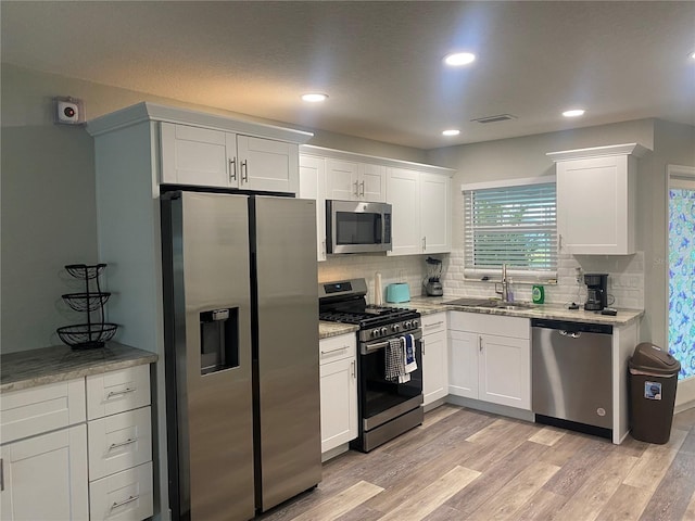 kitchen featuring appliances with stainless steel finishes, a sink, white cabinetry, decorative backsplash, and light stone countertops