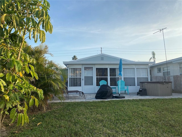 rear view of property with a hot tub, a patio, and a yard