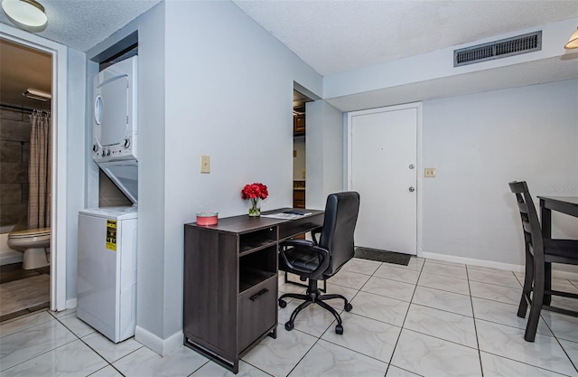 home office with visible vents, a textured ceiling, stacked washing maching and dryer, and baseboards