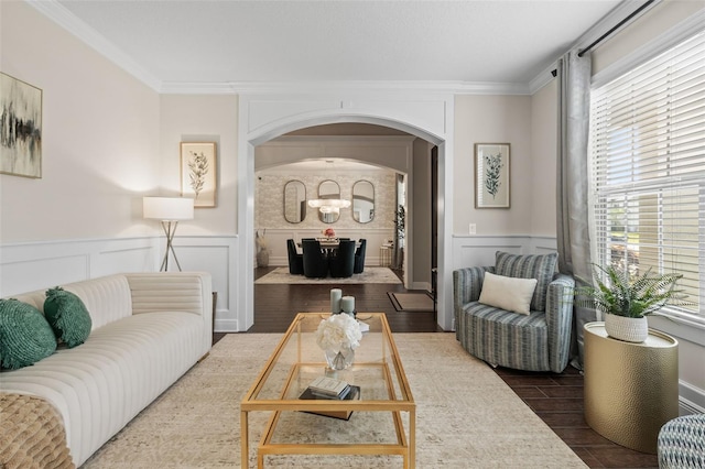 living area featuring arched walkways, crown molding, a wainscoted wall, and wood finished floors