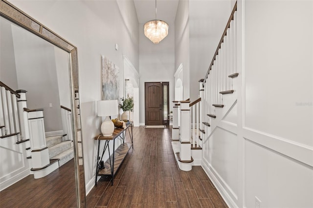 foyer entrance with a towering ceiling, a chandelier, stairway, dark wood finished floors, and a decorative wall
