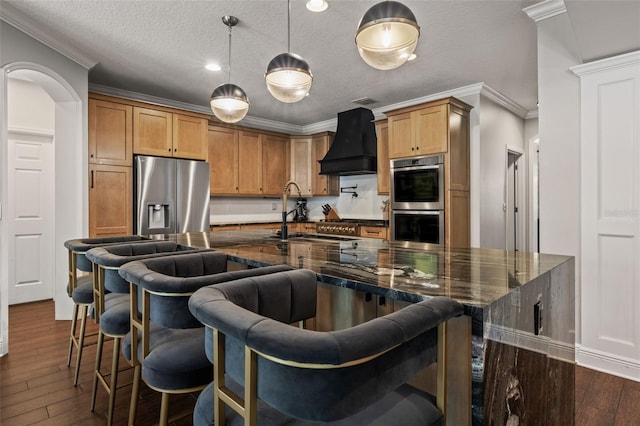 kitchen with ornamental molding, appliances with stainless steel finishes, a sink, custom range hood, and dark wood-style floors