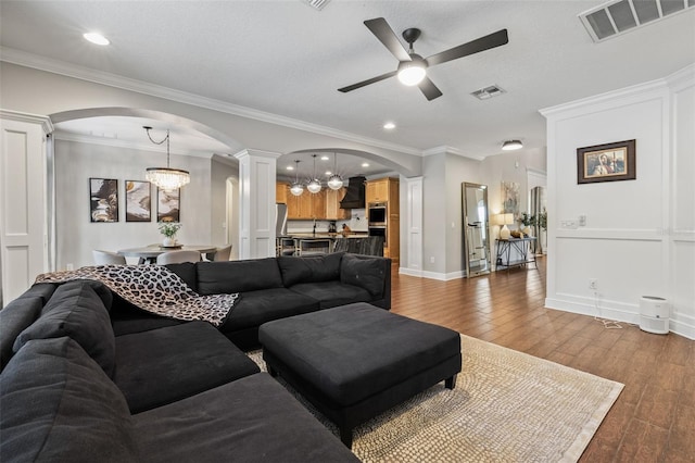 living area featuring arched walkways, ceiling fan with notable chandelier, decorative columns, and visible vents