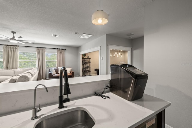 kitchen featuring a sink, open floor plan, ceiling fan, and a textured ceiling