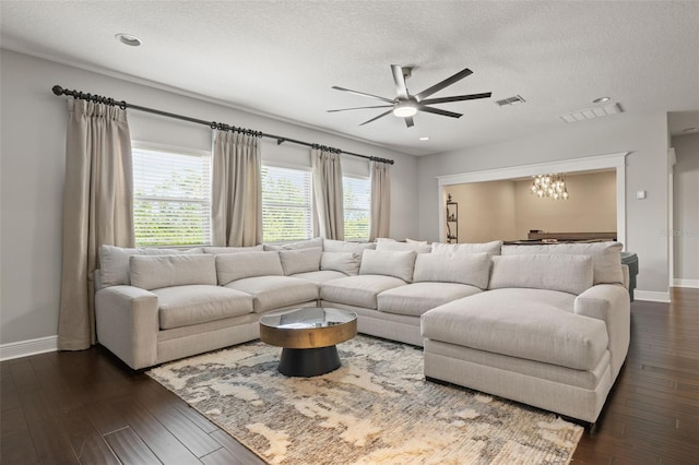 living area featuring ceiling fan with notable chandelier, dark wood-style flooring, visible vents, and a wealth of natural light