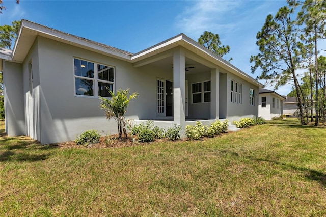 view of side of home with a yard, ceiling fan, and stucco siding