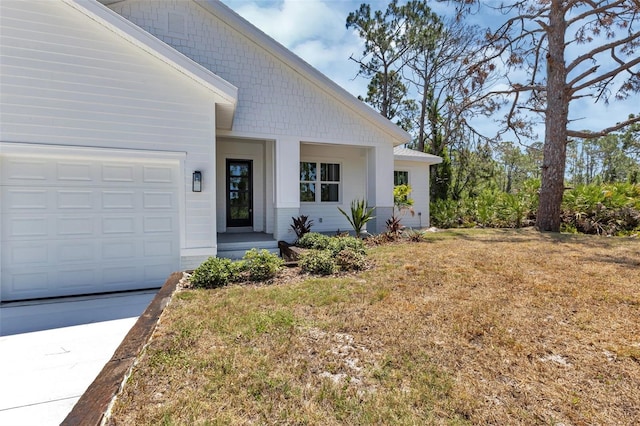 property entrance featuring a lawn, concrete driveway, and a garage