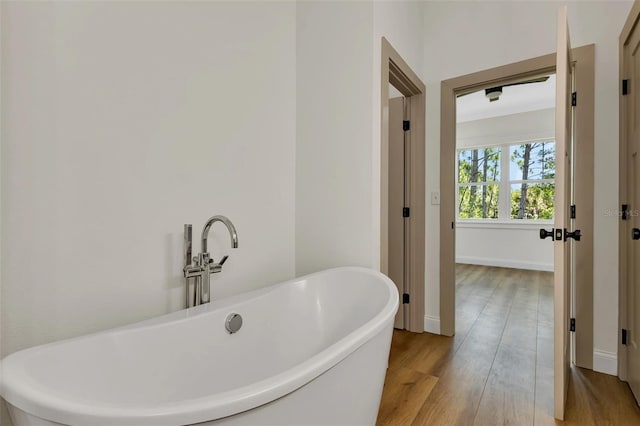 full bathroom featuring baseboards, a soaking tub, and wood finished floors