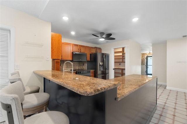 kitchen featuring brown cabinetry, a peninsula, a kitchen breakfast bar, stainless steel fridge with ice dispenser, and a ceiling fan