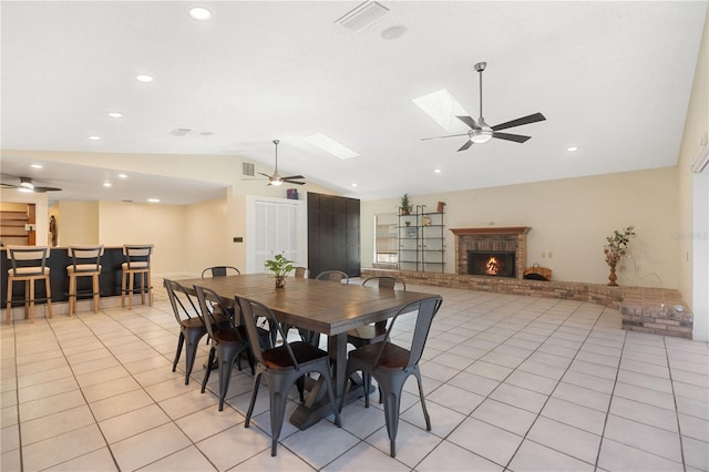 dining room featuring ceiling fan, a brick fireplace, lofted ceiling with skylight, and visible vents