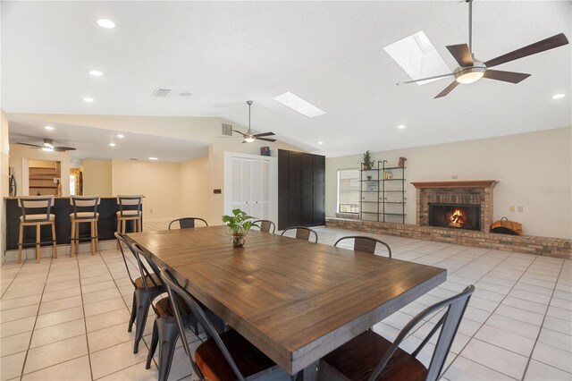 dining space with a brick fireplace, light tile patterned flooring, recessed lighting, and lofted ceiling with skylight